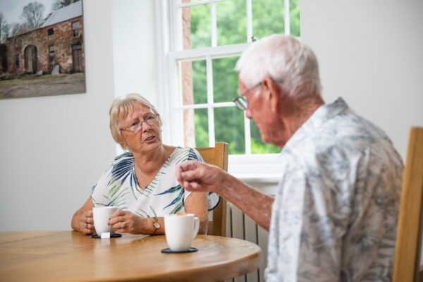 Two senior guests enjoying tea and conversation inside the luxury Independent Apartment at Netherby Hall, Cumbria
