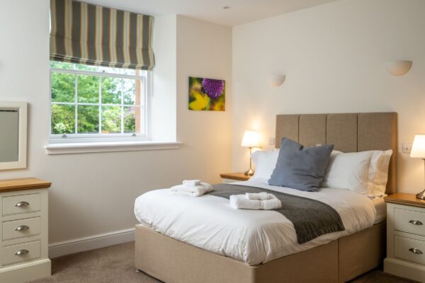 Bedroom in the Independent Apartment at Netherby Hall, featuring a large bed with white linens and a window overlooking green gardens