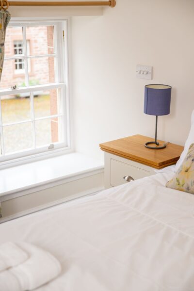 Bedroom in Independent Apartment at Netherby Hall featuring a white bed, wooden nightstand with a purple lamp, and a large window