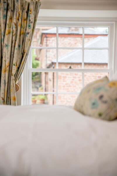 View through a window of the Independent Apartment at Netherby Hall, Cumbria, featuring floral curtains and views of historic brick buildings