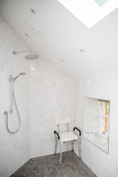 Modern walk-in shower with marble tiles and a shower chair in the Independent Apartment at Netherby Hall