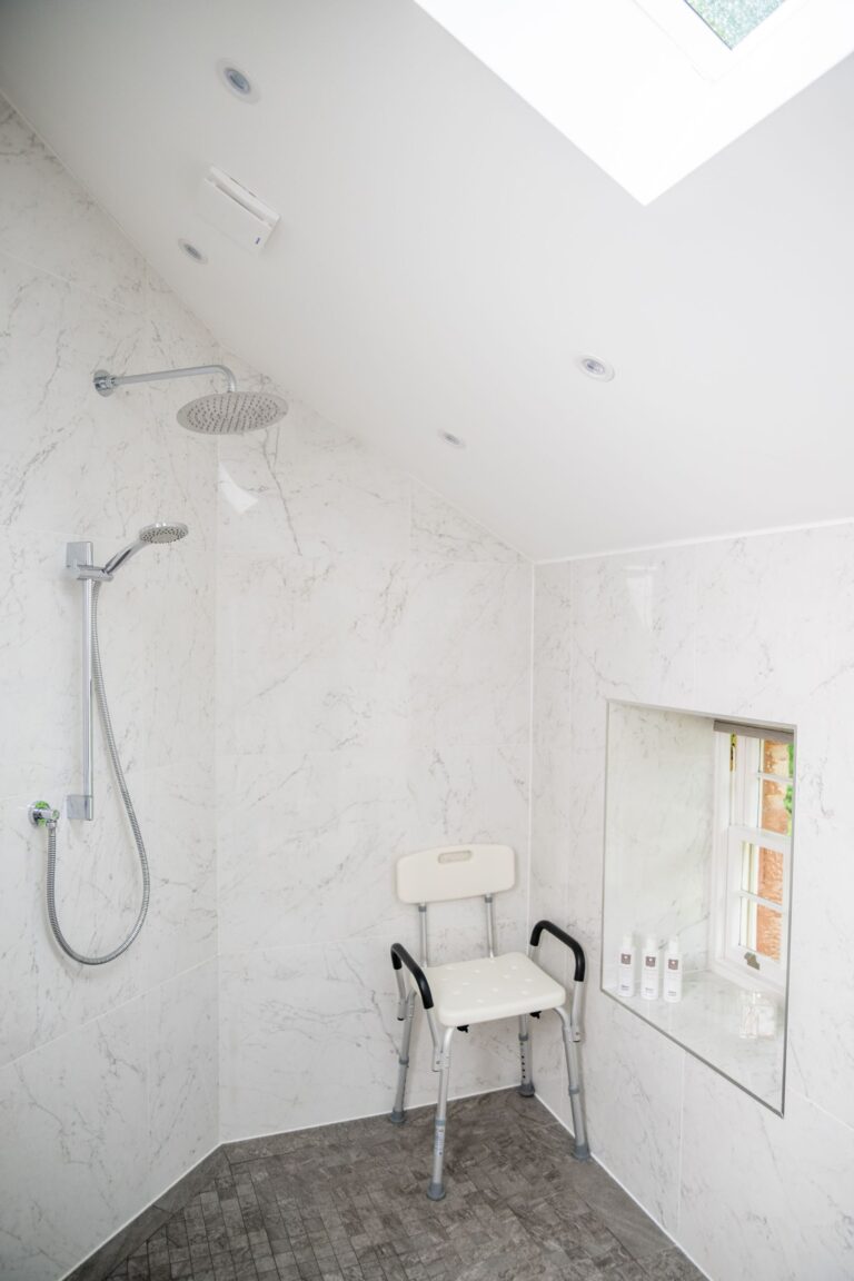 Modern walk-in shower with marble tiles and a shower chair in the Independent Apartment at Netherby Hall
