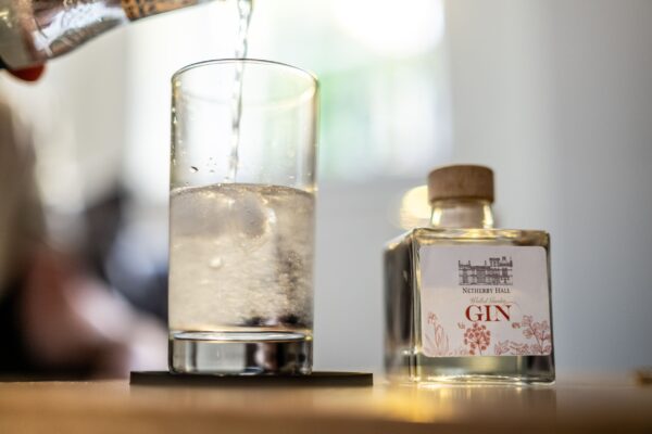 Pouring water into a glass next to a miniature bottle of Netherby Hall Walled Garden Gin at Middle Lodge