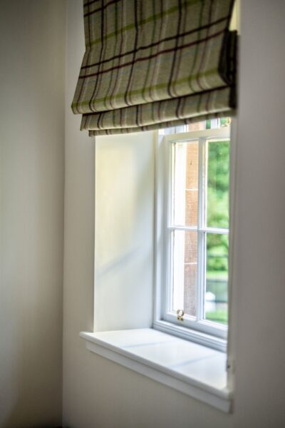 A bright window with a plaid Roman blind overlooking the grounds at Middle Lodge luxury self-catering apartment