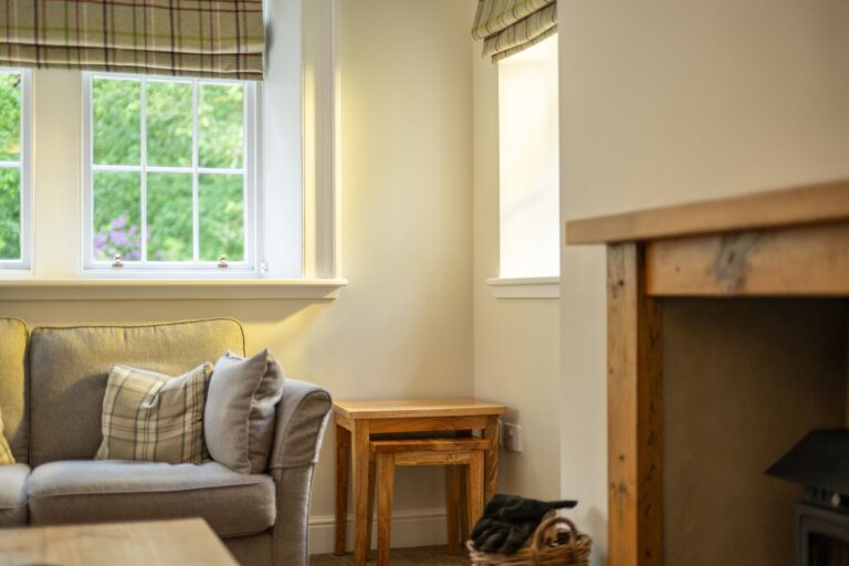 Cozy living room corner in Middle Lodge featuring a grey sofa with plaid cushions and a window view at Netherby Hall