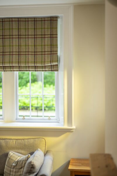 Window with plaid Roman blinds and a view of green trees in the Middle Lodge apartment at Netherby Hall