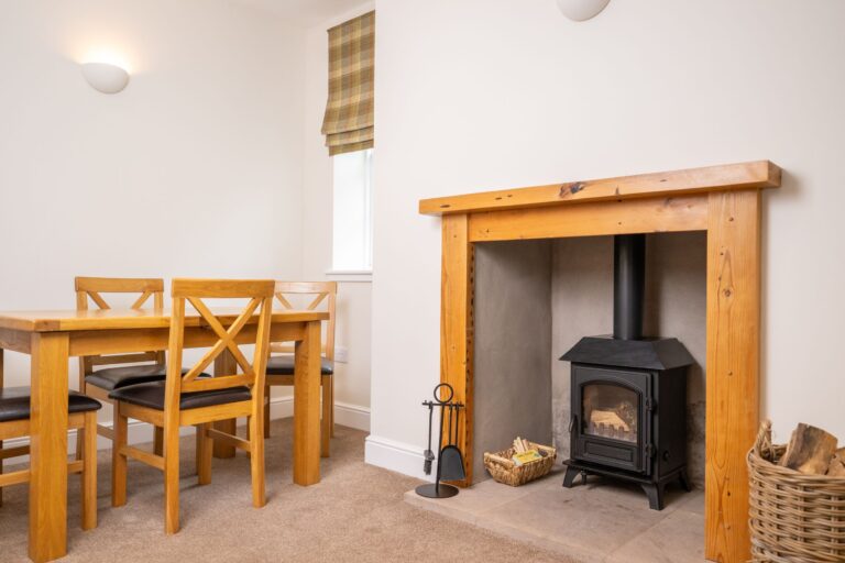 Dining area with a wooden table and chairs next to a modern wood-burning stove and fireplace in Middle Lodge
