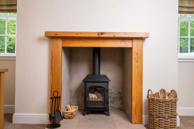 Modern wood-burning stove with a timber mantelpiece in the Middle Lodge apartment at Netherby Hall