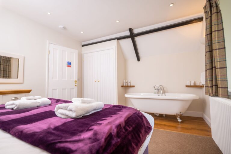 Bedroom at Middle Lodge with a purple throw, white towels, and a freestanding bathtub in a luxury self-catering apartment