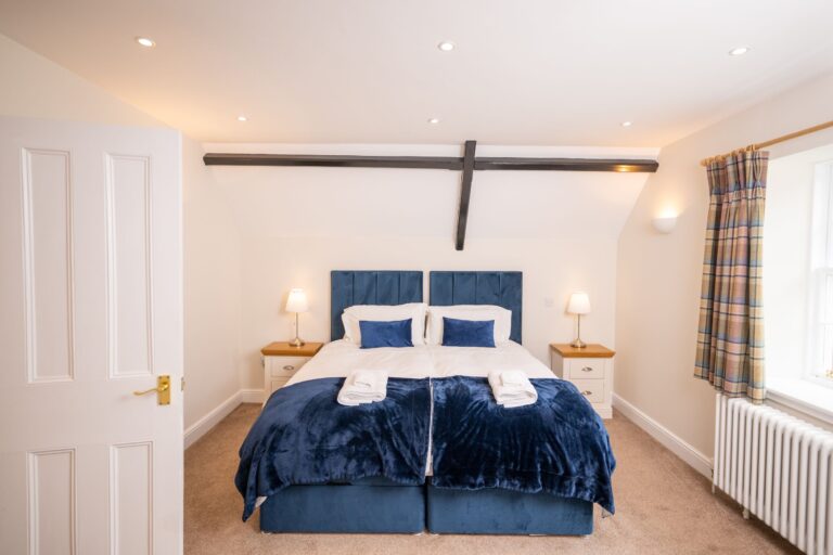 Bedroom at Middle Lodge featuring a plush navy velvet bed, white linens, and rustic wooden ceiling beams at Netherby Hall