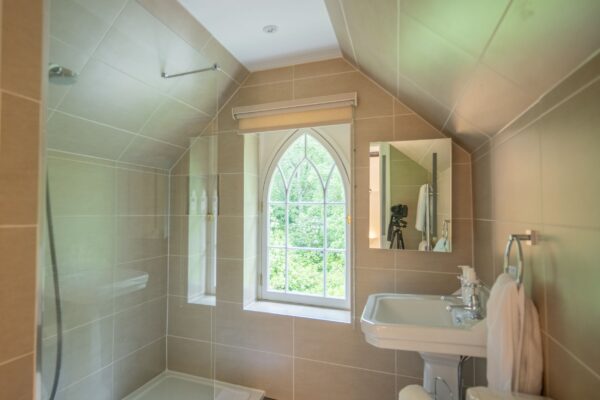 Modern bathroom in Middle Lodge apartment featuring a walk-in shower, white sink, and an arched window with garden views