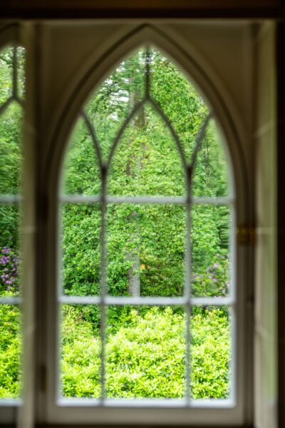 View through a large arched window at Middle Lodge, showing lush green gardens at Netherby Hall