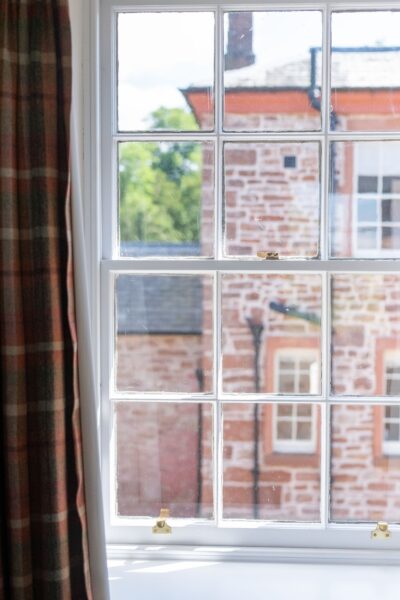View through a multi-pane window in the Salutation Apartment at Netherby Hall, showing historic stone buildings in Cumbria