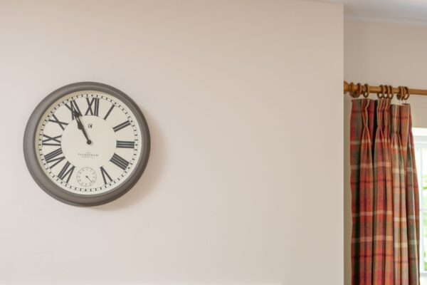 A large round wall clock with Roman numerals hanging in the Salutation Apartment at Netherby Hall