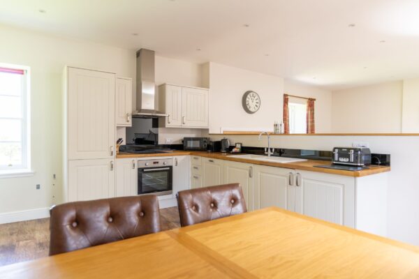 Modern kitchen in Salutation Apartment featuring cream cabinets, wooden countertops, and a dining area with leather chairs at Netherby Hall