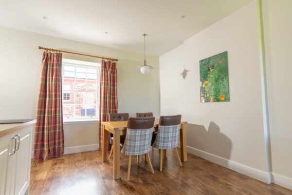 Dining area in Salutation Apartment featuring a wooden table, plaid chairs, and a window with patterned curtains at Netherby Hall