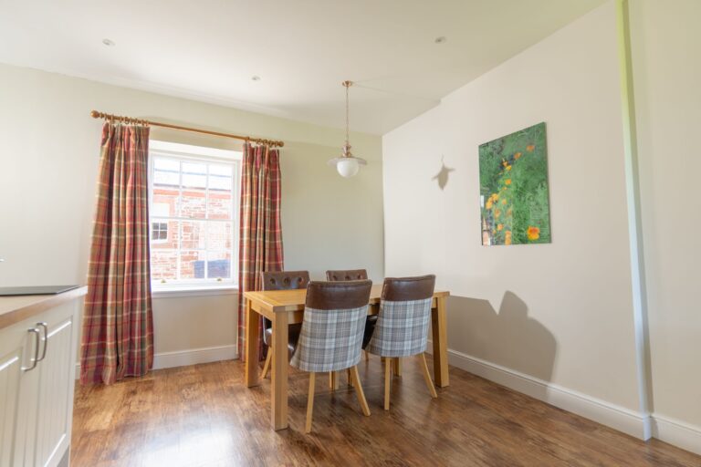 Dining area in Salutation Apartment featuring a wooden table, plaid chairs, and a window with patterned curtains at Netherby Hall