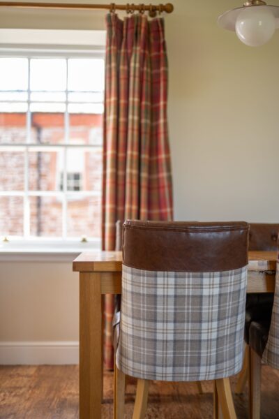 Dining area in the Salutation Apartment featuring a wooden table and plaid upholstered chairs near a large window