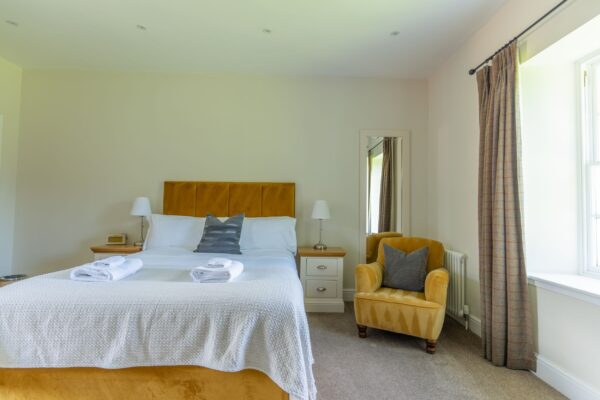 Bright bedroom in the Salutation Apartment at Netherby Hall featuring a double bed with white linens and a yellow armchair