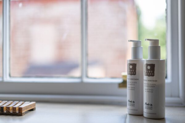 Luxury toiletries including shampoo and conditioner set on a windowsill in Salutation Apartment at Netherby Hall, Cumbria