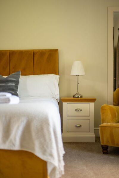 Bedroom in Salutation Apartment featuring a mustard velvet headboard, white bedding, and a modern bedside lamp at Netherby Hall