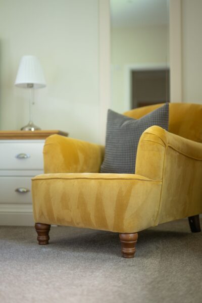 Yellow velvet armchair with a grey checkered cushion in a luxury Salutation Apartment at Netherby Hall, Cumbria