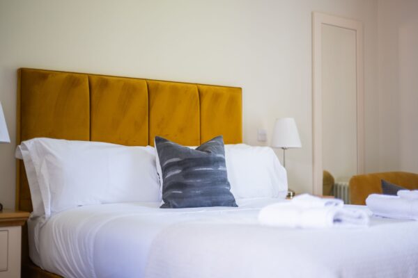 Bedroom in Salutation Apartment at Netherby Hall featuring a mustard yellow velvet headboard and white linens in luxury Cumbria accommodation