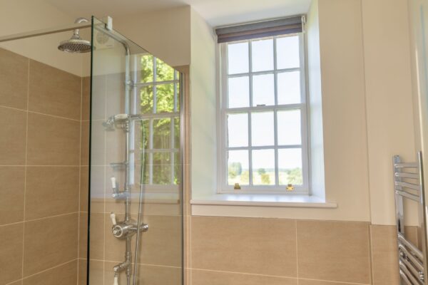Modern bathroom in the Salutation Apartment at Netherby Hall featuring a glass shower and large window with countryside views