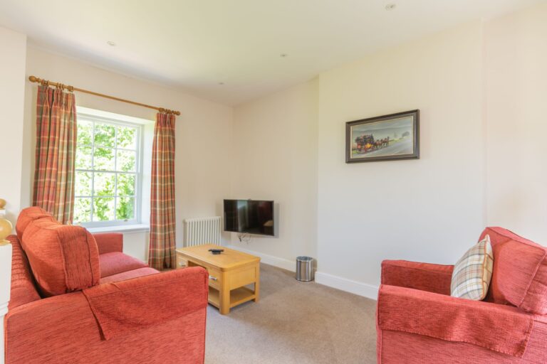 Living room in Salutation Apartment featuring red armchairs, a wooden coffee table, a television, and a window with plaid curtains