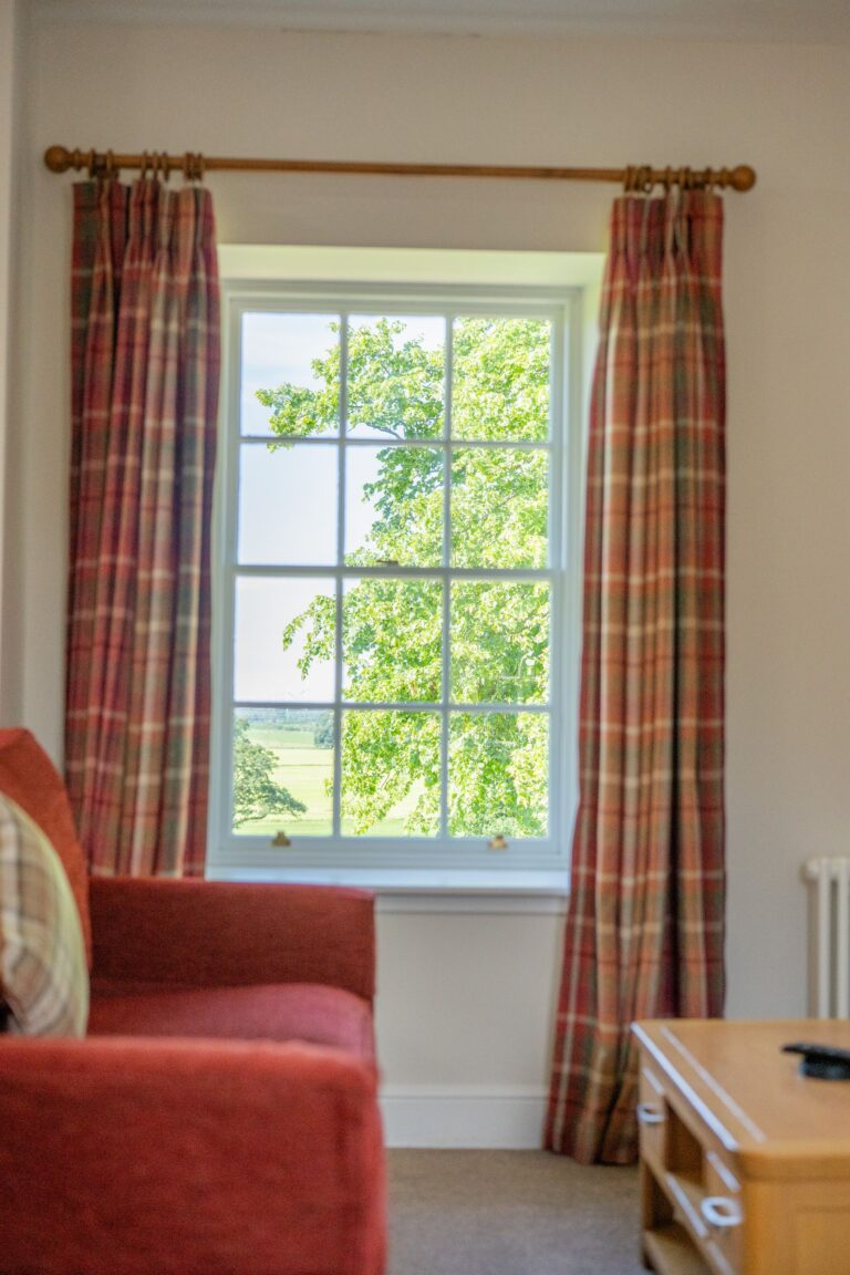 Window with view of green trees and garden from inside the Salutation Apartment at Netherby Hall, Cumbria