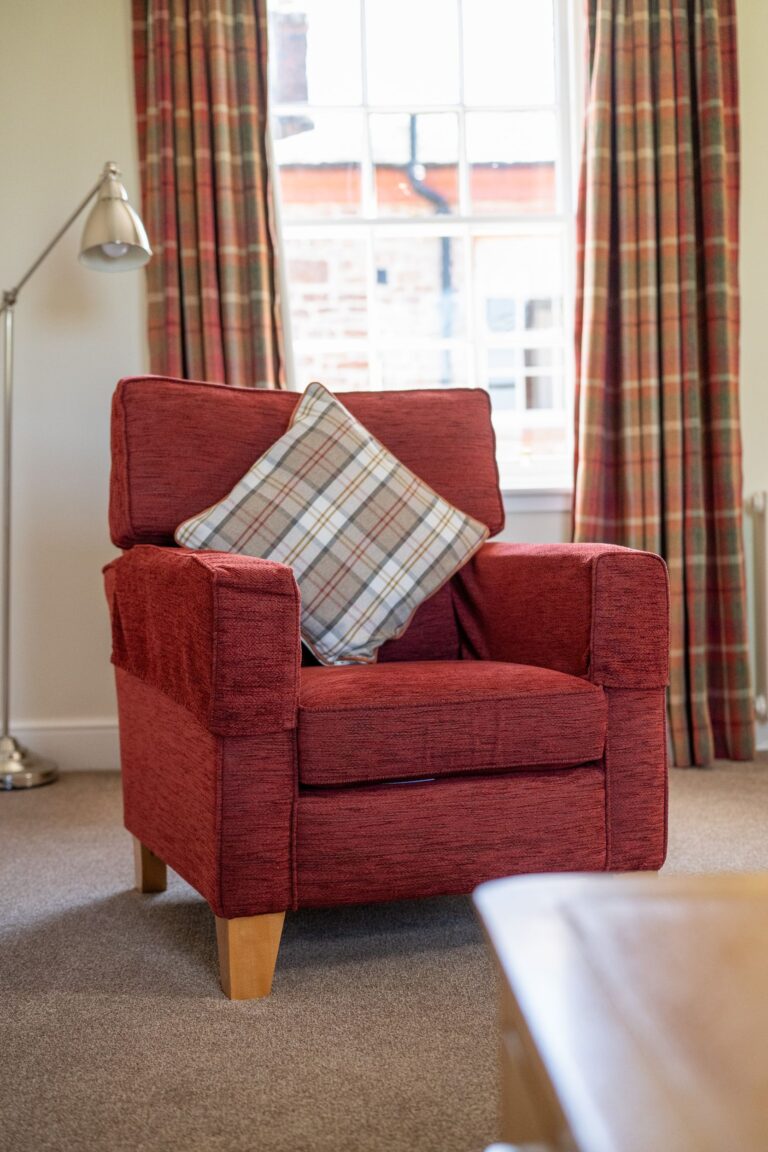 Red armchair with a plaid cushion in the Salutation Apartment at Netherby Hall, Cumbria