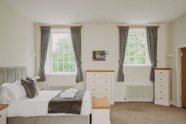 Bright and airy bedroom in the Sir Walter Scott Apartment featuring a large bed, white chest of drawers, and large windows at Netherby Hall