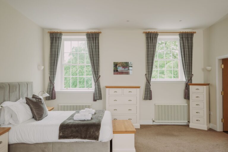 Bright and airy bedroom in the Sir Walter Scott Apartment featuring a large bed, white chest of drawers, and large windows at Netherby Hall