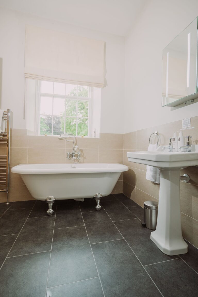 Modern bathroom in the Sir Walter Scott Apartment featuring a white clawfoot bathtub and pedestal sink with grey tiled flooring