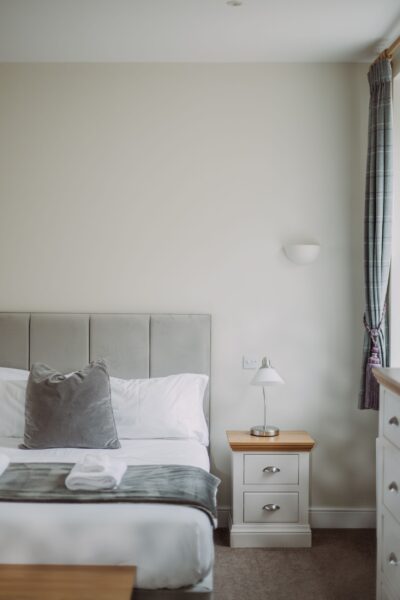 Bedroom interior of Sir Walter Scott Apartment featuring a neatly made bed with a grey velvet pillow and a white bedside lamp