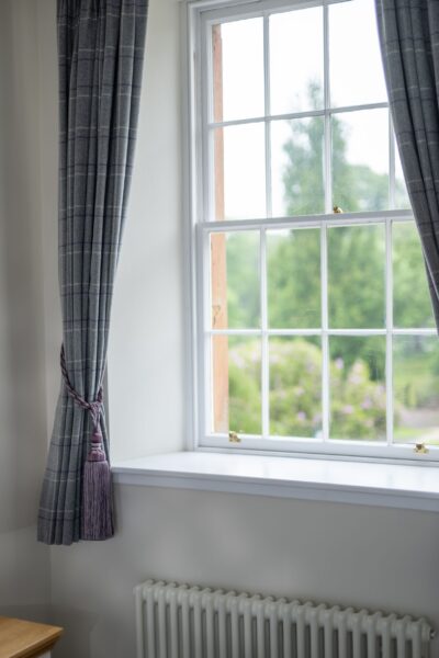 A window with white frames and grey plaid curtains in the Sir Walter Scott Apartment at Netherby Hall, Cumbria