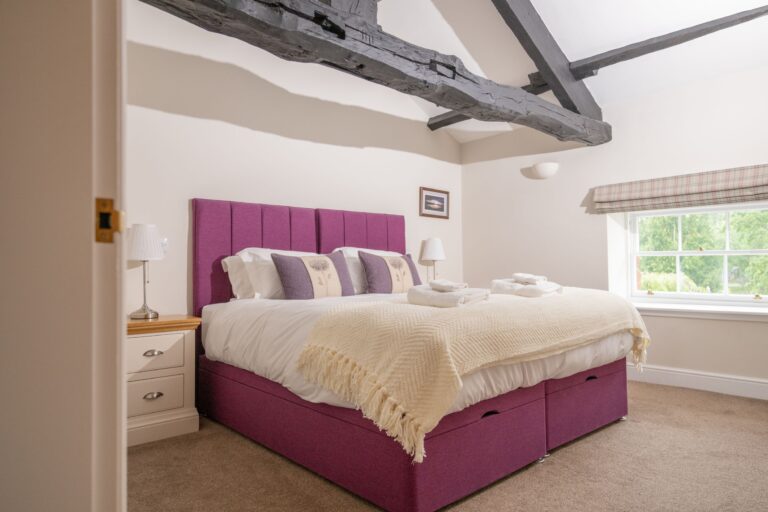 Bedroom in the luxury Sir Walter Scott Apartment at Netherby Hall featuring a purple upholstered bed and rustic wooden ceiling beams