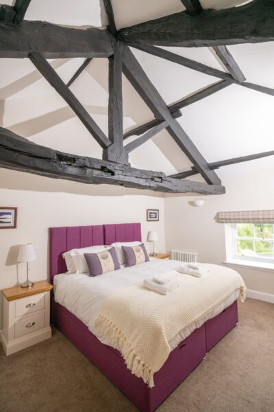 Bedroom in Sir Walter Scott Apartment featuring a large bed with purple headboard and rustic exposed wooden ceiling beams at Netherby Hall