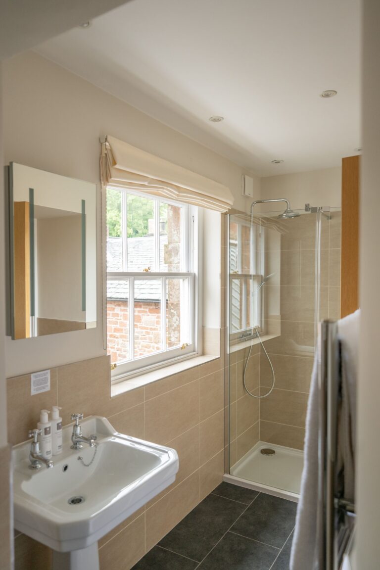 Modern bathroom in the Sir Walter Scott Apartment featuring a white pedestal sink, walk-in glass shower, and large window at Netherby Hall