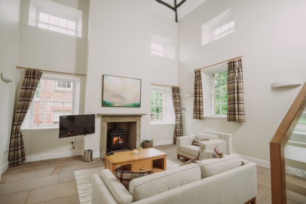 Modern living room in Sir Walter Scott Apartment featuring a fireplace, neutral decor, and large windows at Netherby Hall, Cumbria