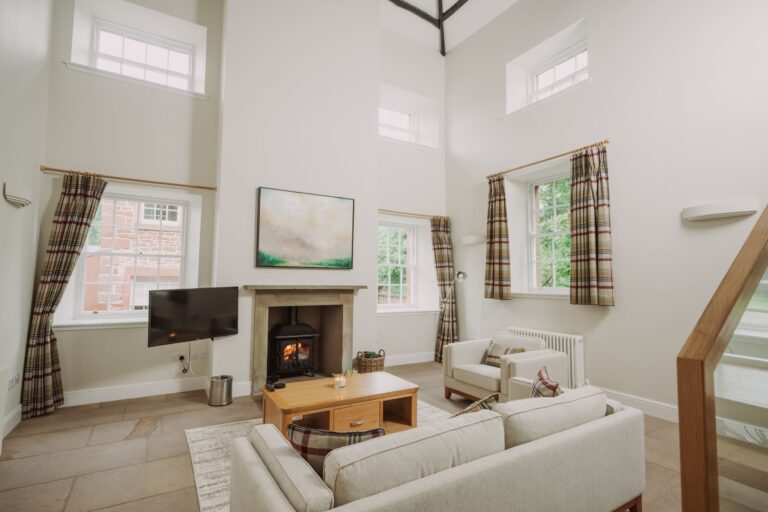 Modern living room in Sir Walter Scott Apartment featuring a fireplace, neutral decor, and large windows at Netherby Hall, Cumbria