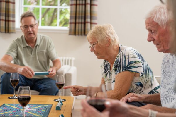 Elderly friends enjoying games and wine inside a luxurious Sir Walter Scott Apartment at Netherby Hall, Cumbria