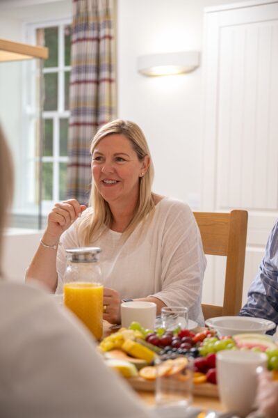 Smiling woman enjoying breakfast with fresh fruit and juice at the Sir Walter Scott Apartment in Netherby Hall, Cumbria
