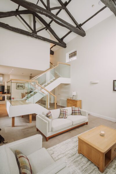 Modern living room in Sir Walter Scott Apartment featuring exposed timber beams, a white sofa, and a glass staircase