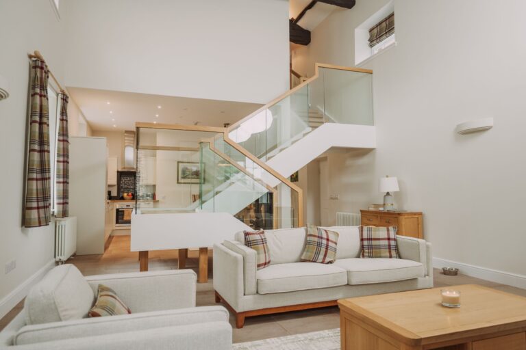 Modern living room in Sir Walter Scott Apartment featuring a white sofa with plaid cushions, a wooden coffee table, and a glass staircase