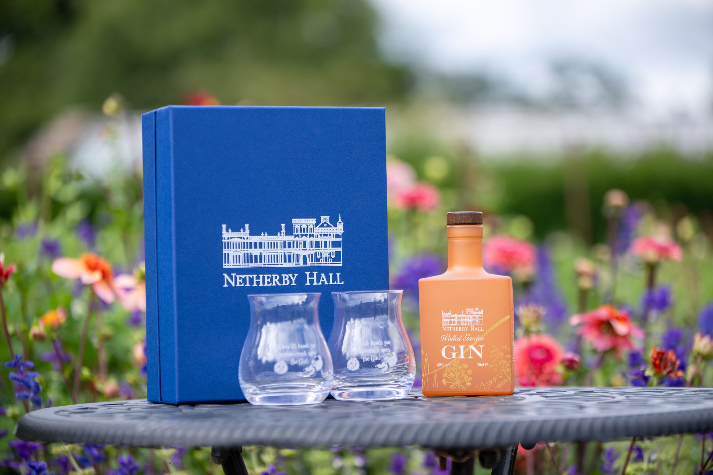 Netherby Hall gin bottle and blue gift box with glasses set against a lush garden background Netherby Hall gin gift set with a blue branded box and two glasses set against a lush garden background