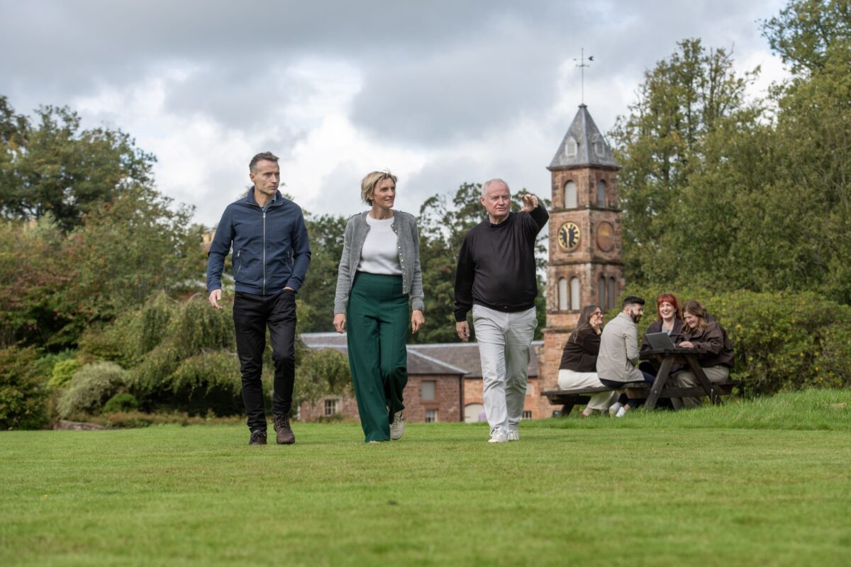 People walking across a lawn at Netherby Hall with a brick clock tower and colleagues working at a picnic table