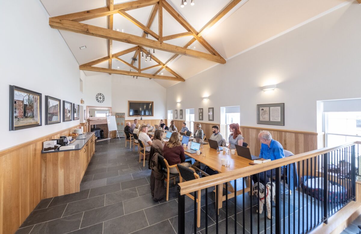 Conference room at Netherby Hall with exposed timber trusses and a long wooden table where guests use laptops during an event