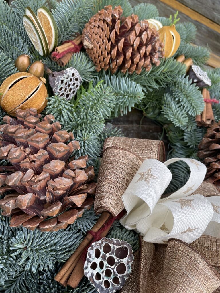 Close-up of a festive Christmas wreath with pine cones, dried oranges, cinnamon sticks and gold star ribbon bow