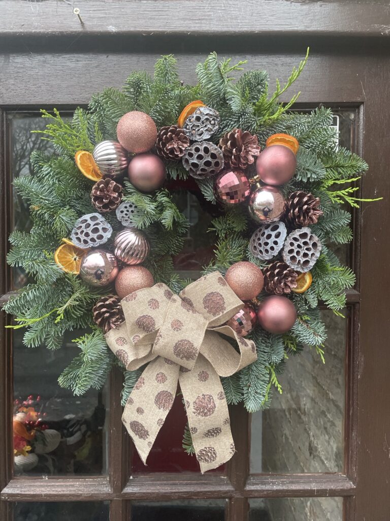 Festive Christmas wreath with pinecones, dried orange slices, rose-gold baubles and a burlap bow hung on a wooden door at Netherby Hall.
